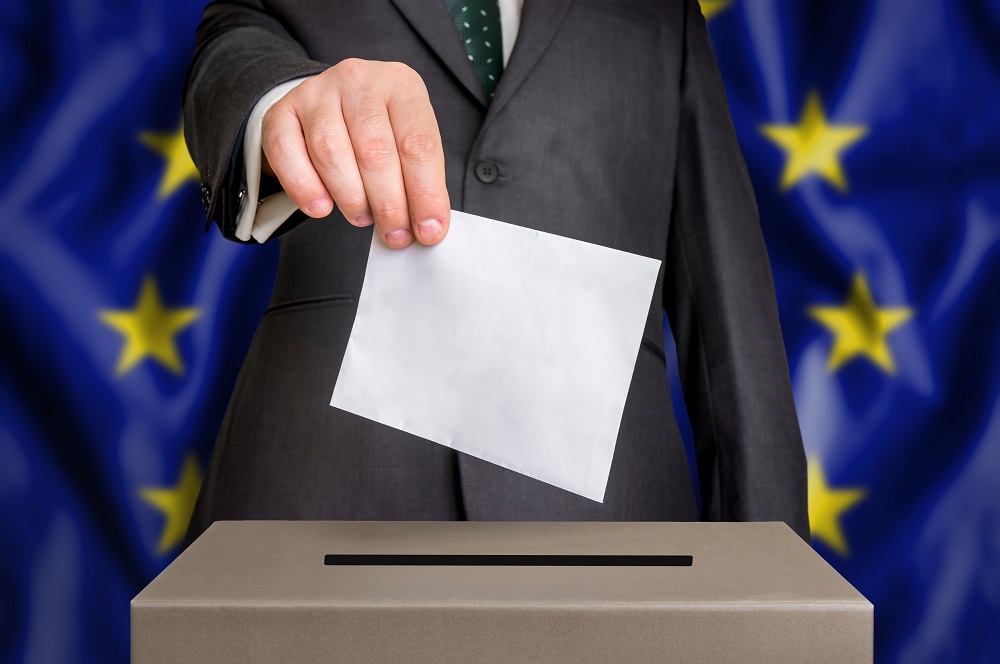 Election in European Union - voting at the ballot box. The hand of man putting his vote in the ballot box. Flag of EU on background.
