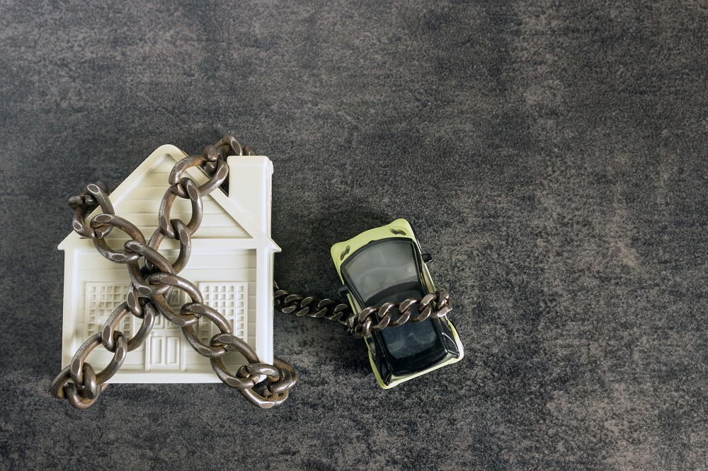 Small white house, car and a decorative chain on a dark background. Concept - risks, lose property, seize, mortgage.